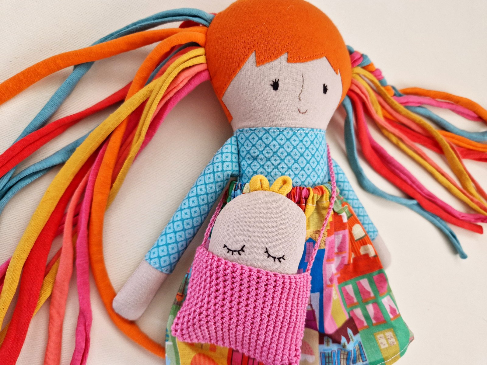 Cloth doll wearing a colorful dress, pink leggings, and a knitted handbag.