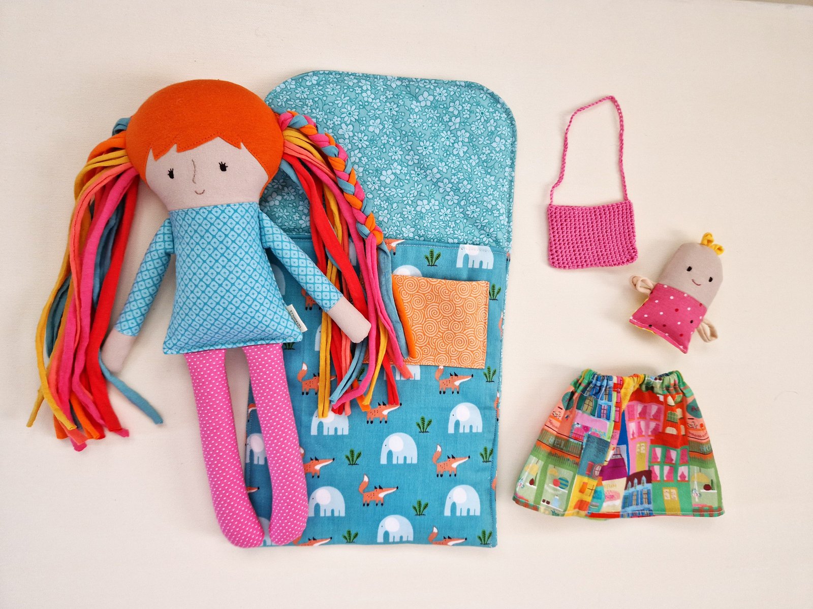 Fabric doll with colorful hair displayed beside a fabric bag, skirt, and small handbag.