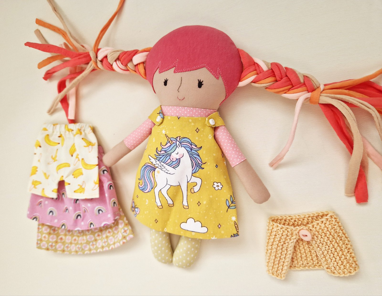 Soft play doll with multicolored braids and a bright yellow unicorn-themed outfit.