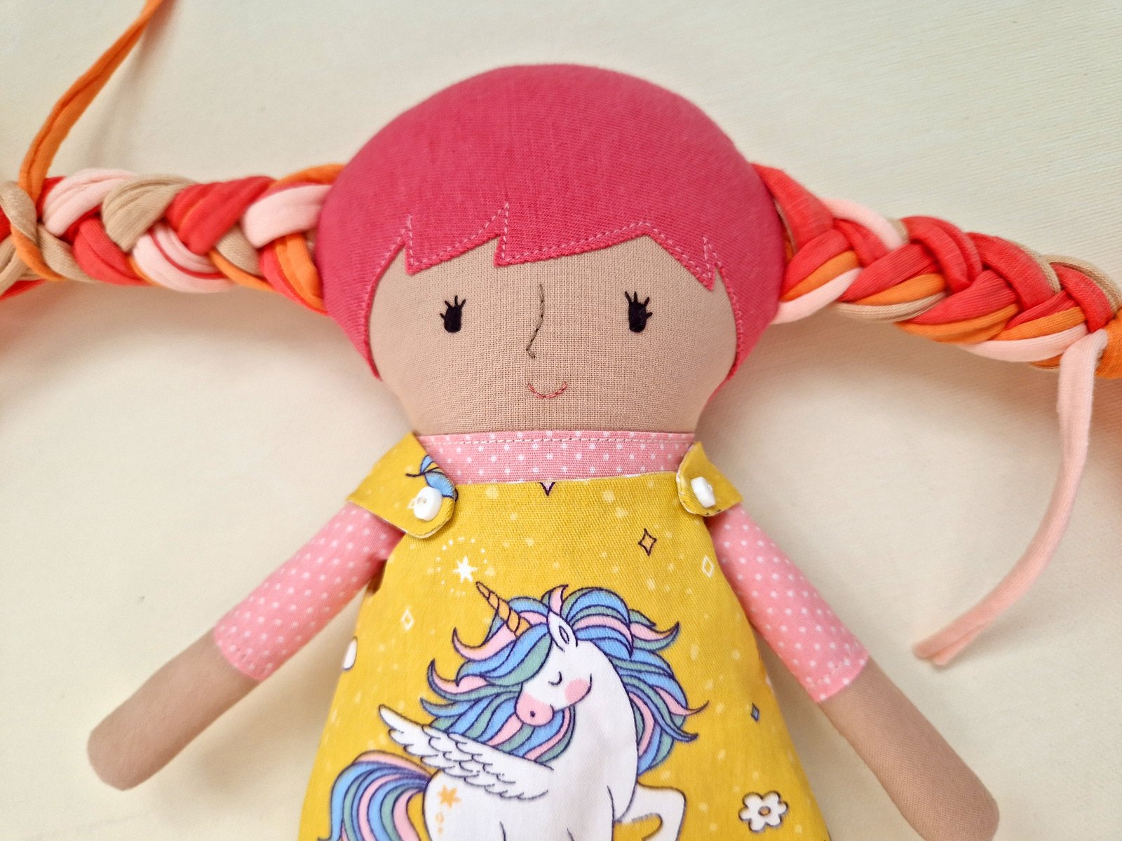 Children's cloth doll wearing a colorful yellow dress with additional clothes in the background.