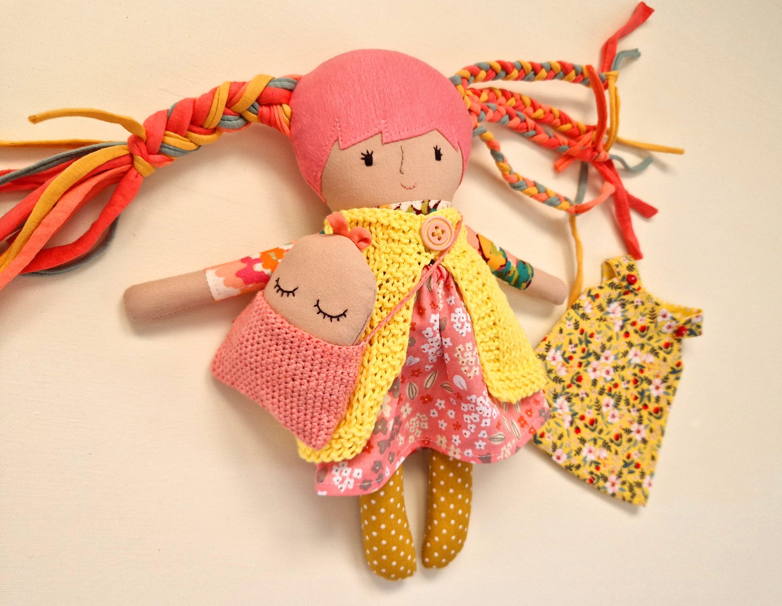 Soft play doll with polka dot leggings and a yellow knitted vest beside her.