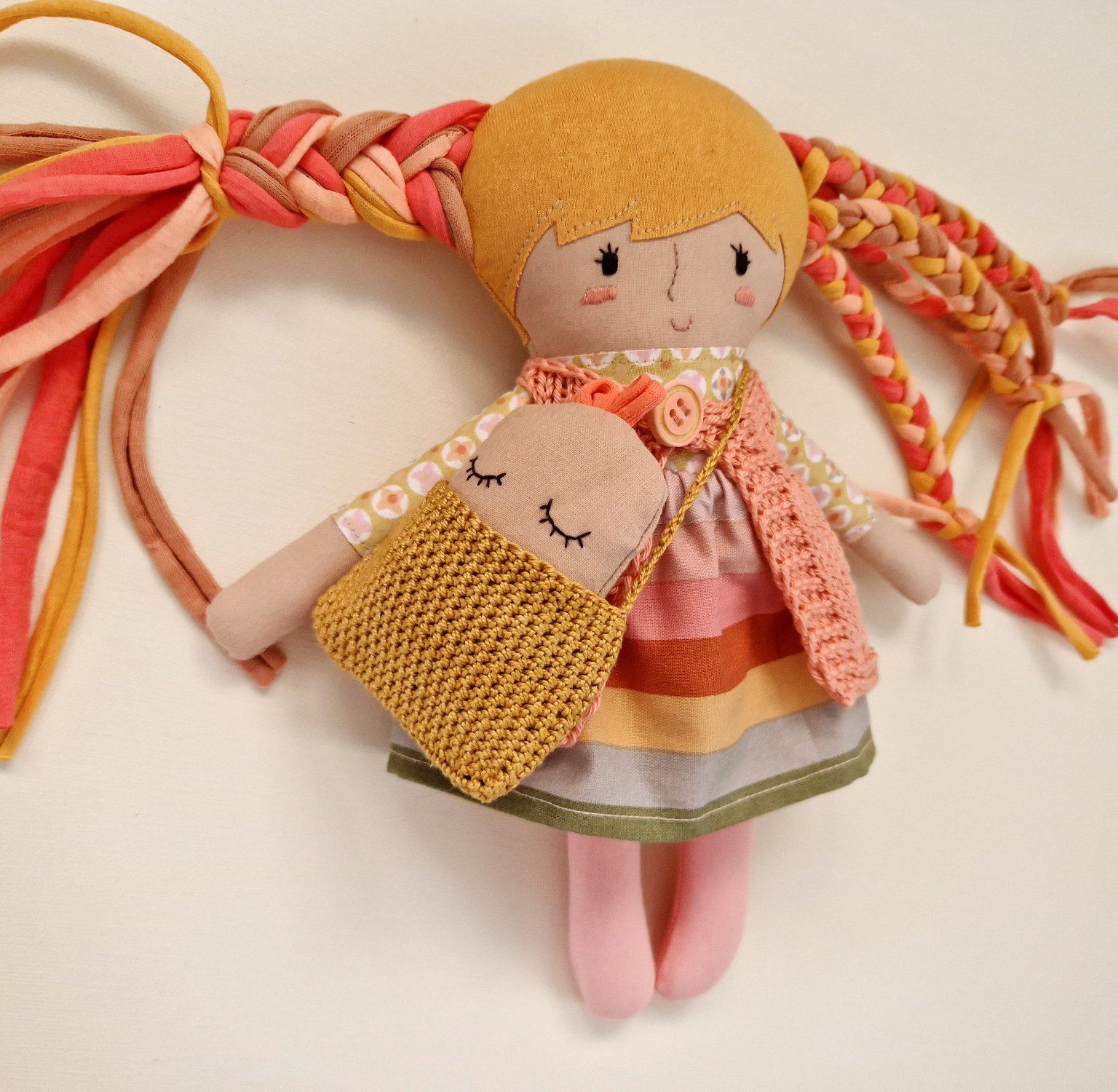 Fabric doll wearing a floral dress and holding a baby doll with a heart print.