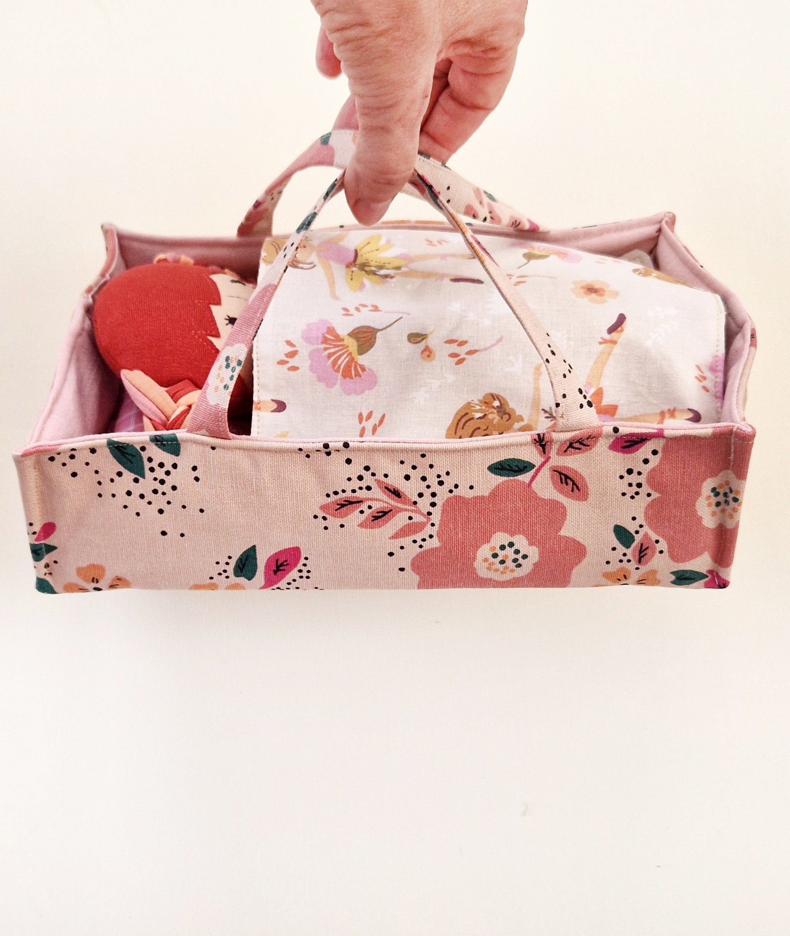 Fabric doll with long hair in pink and red tones displayed beside clothes and a fabric bag.