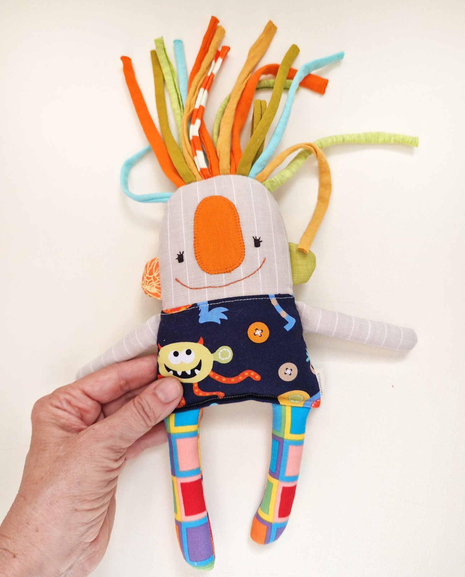 Handmade textile art doll with colorful fabric hair and a dark skirt featuring a playful monster