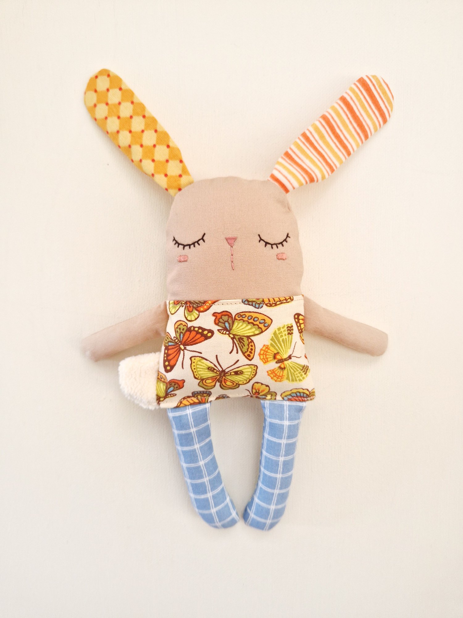 Handmade baby bunny toy with sleepy embroidered face and blue checkered legs