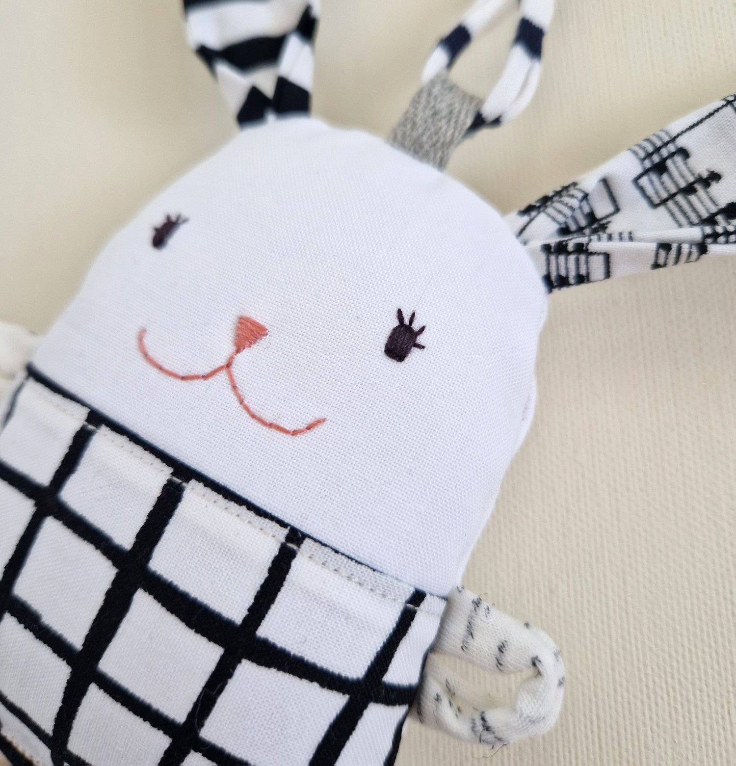 Soft textile bunny rattle with sleeping face, striped ears and wooden ring